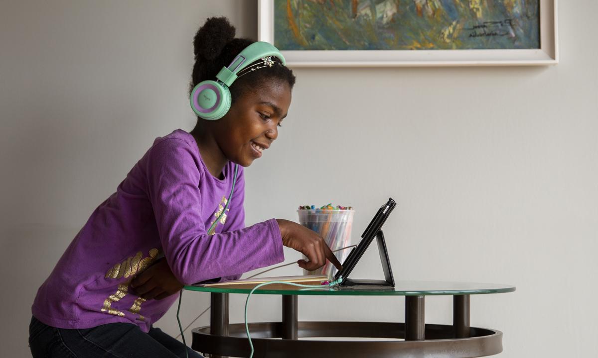 一个小孩戴着耳机坐在电脑前微笑的画面