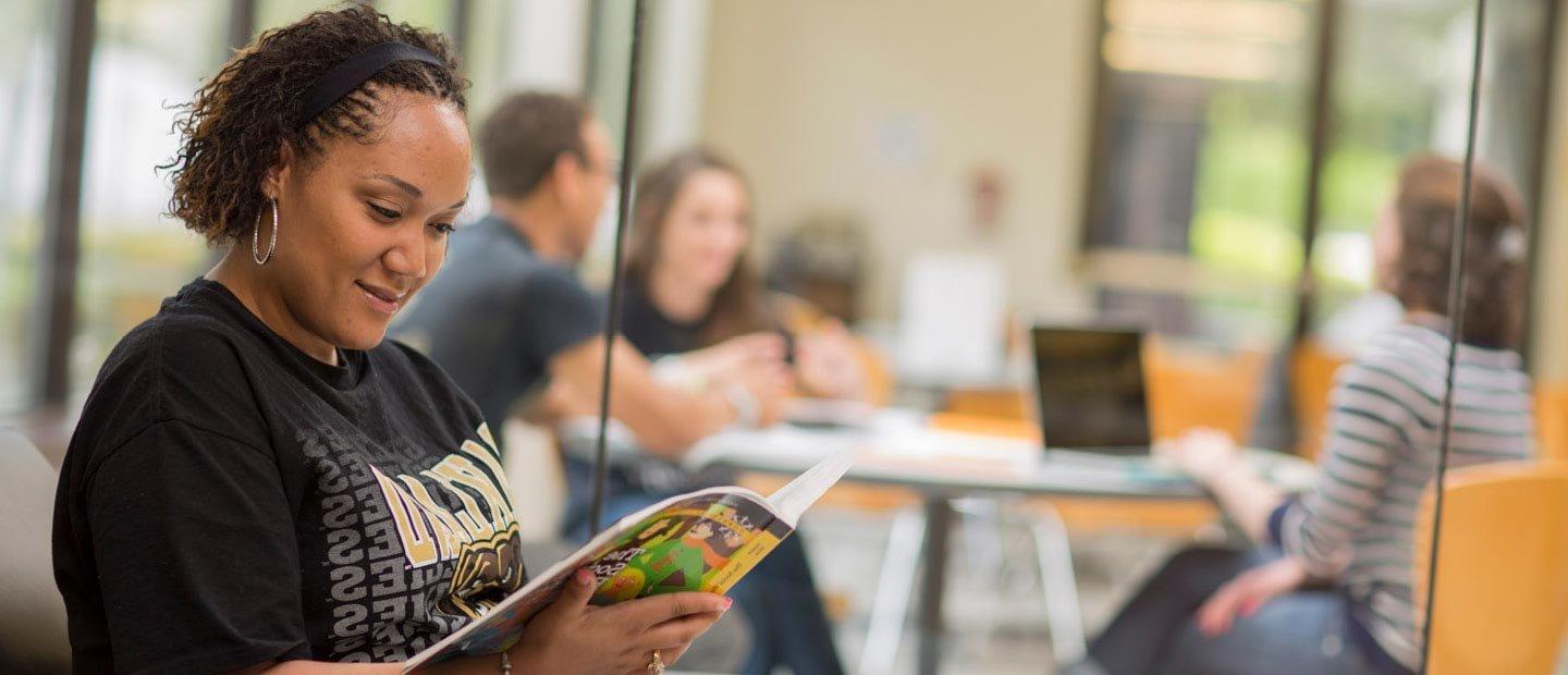 female student wearing a black Oakland University shirt, reading a book