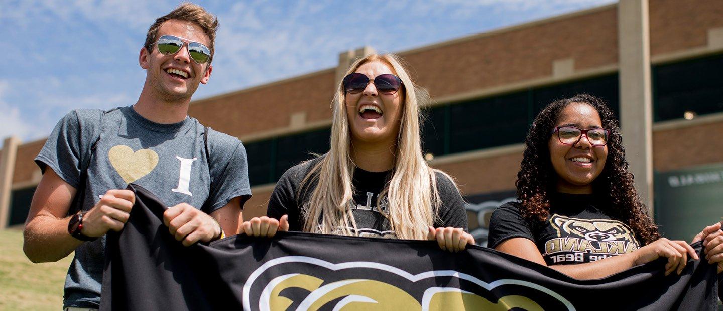 三名俄亥俄大学的学生举着一面黑色的旗帜，上面有金色的棕熊头吉祥物.